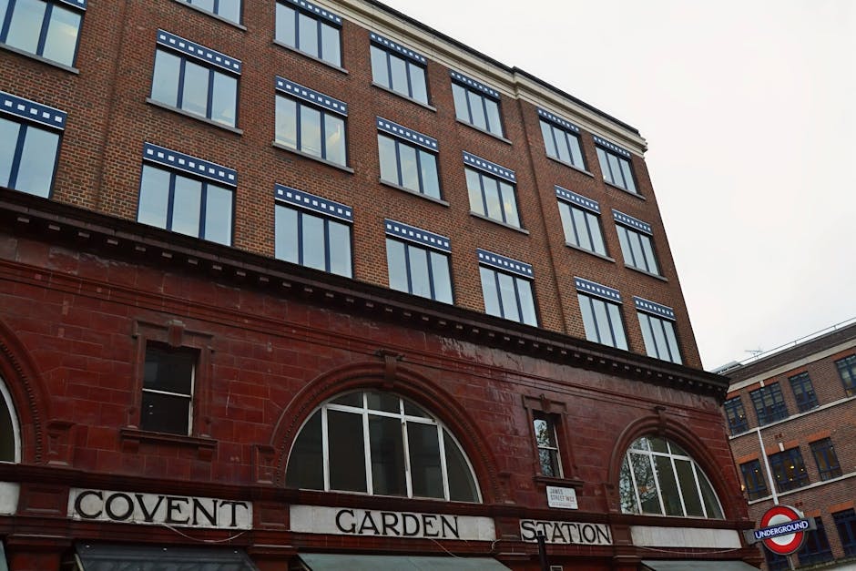 A multi-story brick building with large rectangular windows featuring decorative blue and white accents at the top of each window frame, situated above a red brick storefront with arched windows and t